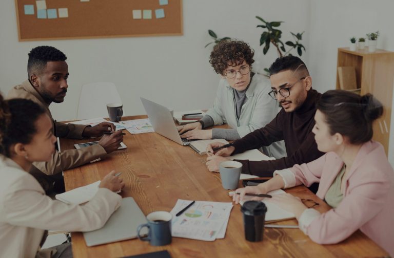 A diverse group of professionals collaborating around a wooden table with laptops and notebooks.